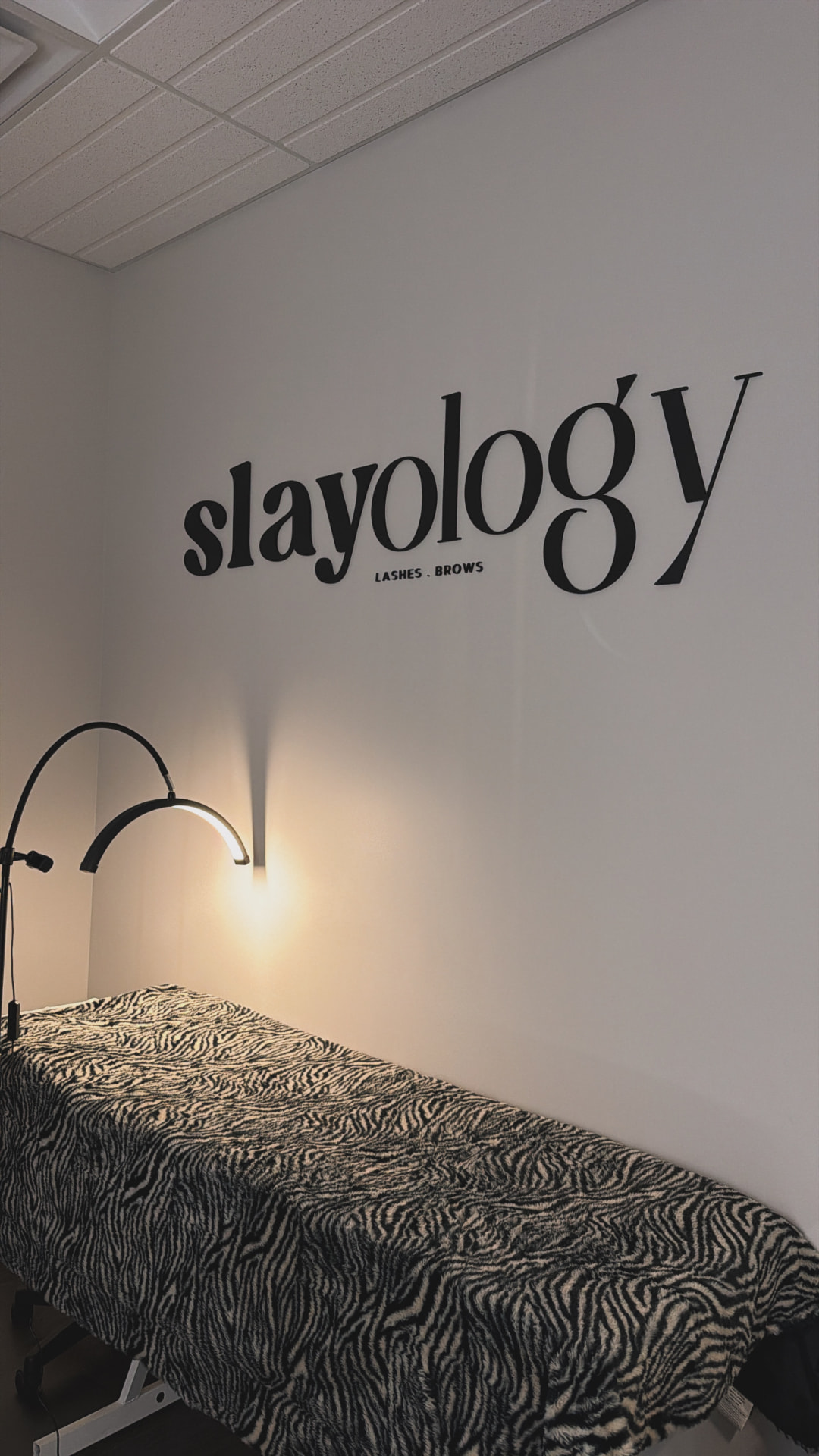 Slayology studio wall with logo above a lash bed under warm light